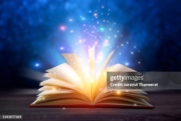 bewitched book with magic glows in the darkness set on a wooden table - library old books stock-fotos und bilder