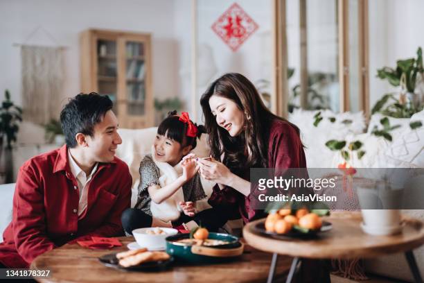 lovely daughter chatting joyfully with father and mother and enjoying family bonding time while celebrating chinese new year at home - chinese new year stock pictures, royalty-free photos & images