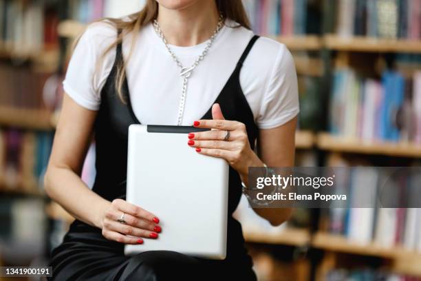 middle section librarian woman holding tablet against blurred library background - red nail polish stock-fotos und bilder