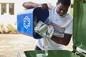 Young Man Emptying Household Recycling Into Green Bin