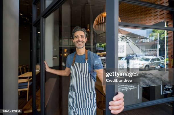 happy waiter opening the doors of a restaurant and smiling - bar reopening stock pictures, royalty-free photos & images