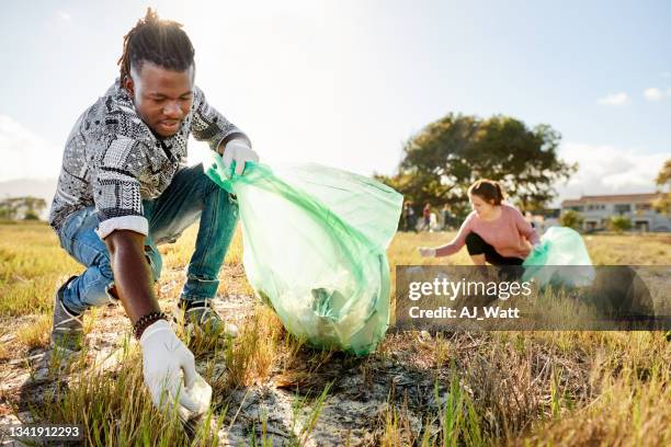 two volunteers picking up garbage in a field during a community cleanup day - picking up garbage stock pictures, royalty-free photos & images