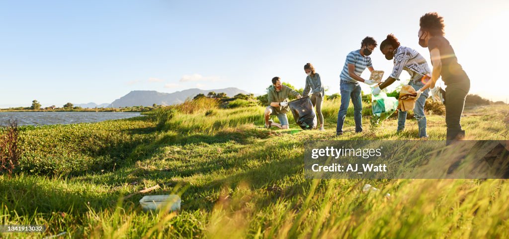 Volunteers in masks collecting litter in a nature reserve by a river