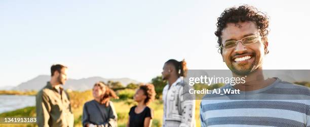 smiling young man standing in a field with friends in the background - glases group nature stock pictures, royalty-free photos & images