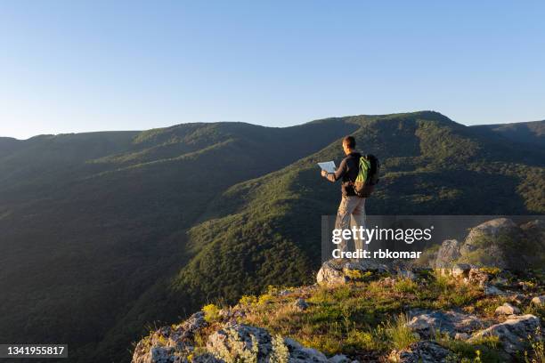 traveler reading map while standing on edge of mountain range at sunrise - climbing plant stock-fotos und bilder