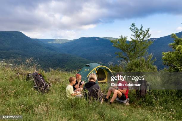 family enjoying eating when trekking with tent in mountains - camping photos et images de collection
