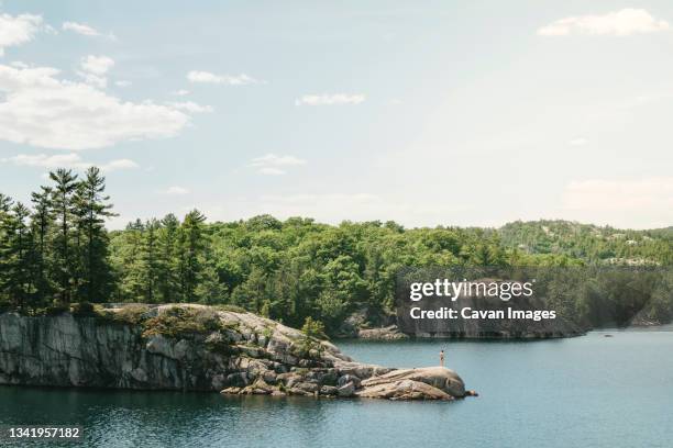 distant view of young woman standing on a rock in the middle of george lake - killarney canada stockfoto's en -beelden