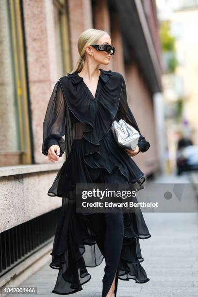 Leonie Hanne wears black Gucci sunglasses, silver earrings, a black silk puffy sleeves / buttoned V-neck / ruffled long train shirt, black slit /...