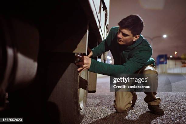 early 30s truck driver checking rear tire at night - vrachtwagen banden stockfoto's en -beelden