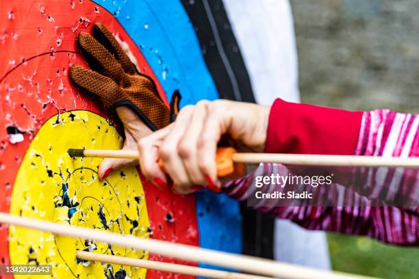 a female archer remove arrows from a target on an archery field - archery target stock pictures, royalty-free photos & images