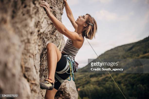 young woman rock climbing on the cliff - trepar imagens e fotografias de stock