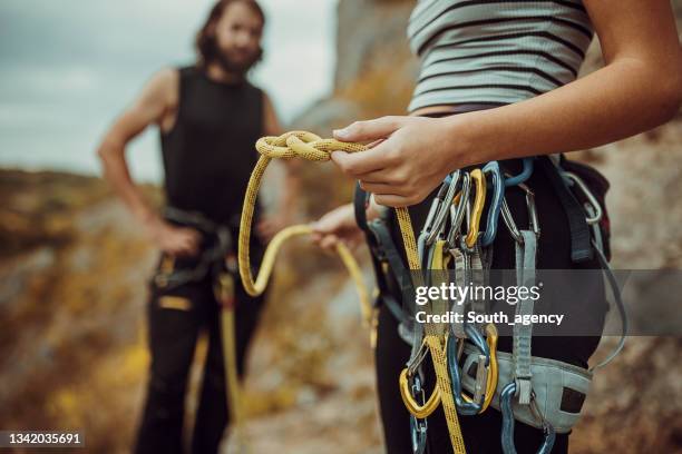 couple enfile du matériel d’escalade, noue des nœuds pour le harnais de sécurité et se prépare pour l’escalade - mousqueton photos et images de collection