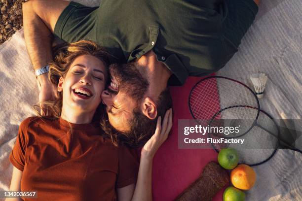 happy young couple, lying on the picnic blanket, sharing affectionate to each-another, celebrating their love - romantic picnic stockfoto's en -beelden