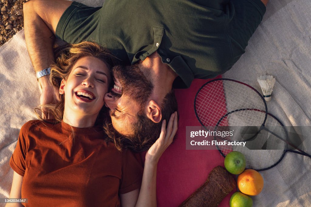 Happy young couple, lying on the picnic blanket, sharing affectionate to each-another, celebrating their love