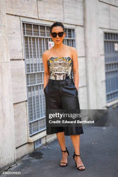 Guest wears black sunglasses, a gold necklace, a black / beige / yellow / gray print pattern off-shoulder body jumpsuit / top, black shiny leather...