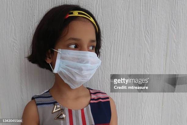 close-up image of medical face mask being worn indoors by young indian girl, protection against and to prevent the spread of coronavirus covid-19 virus during global health emergency - arenavirus stock pictures, royalty-free photos & images