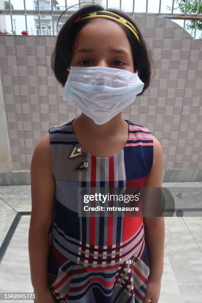 image of medical face mask being worn indoors by young indian girl, protection against and to prevent the spread of coronavirus covid-19 virus during global health emergency - arenavirus stock pictures, royalty-free photos & images