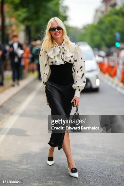 Guest wears black vintage sunglasses, a white with black task pattern puffy sleeves / knotted neck shirt, a black silk high waist corset / long slit...