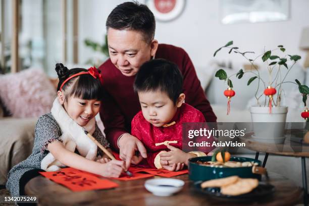 自宅で祖父と夫婦で中国の旧正月ファイチュン(縁起の良いメッセージ)のための中国の書道を練習する喜びの小さな孫娘と孫 - couplets ストックフォトと画像