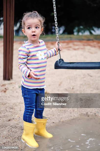 a 3 year old girl in yellow boots is playing with her rubber duck in a puddle - schaukel regen stock-fotos und bilder