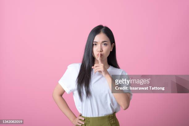 index finger on lips, silence gesture, shhh quiet, asks for voicelessness forefinger at the mouth. young attractive woman in a light t-shirt on pink background - shhh finger stock pictures, royalty-free photos & images