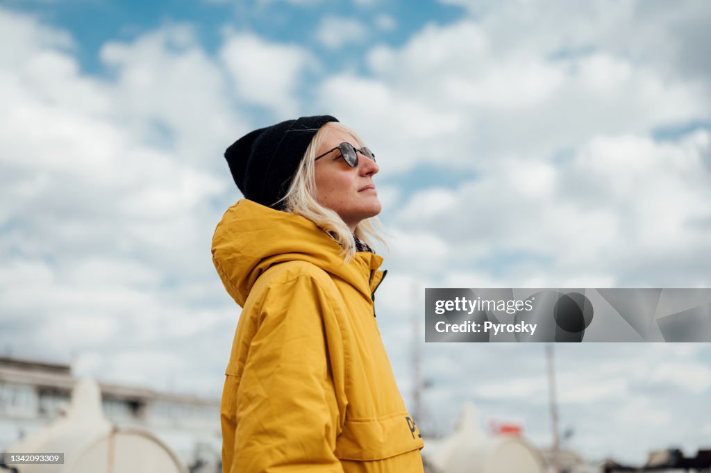 Eine urbane junge Frau in gelber Jacke gegen blauen Himmel 1