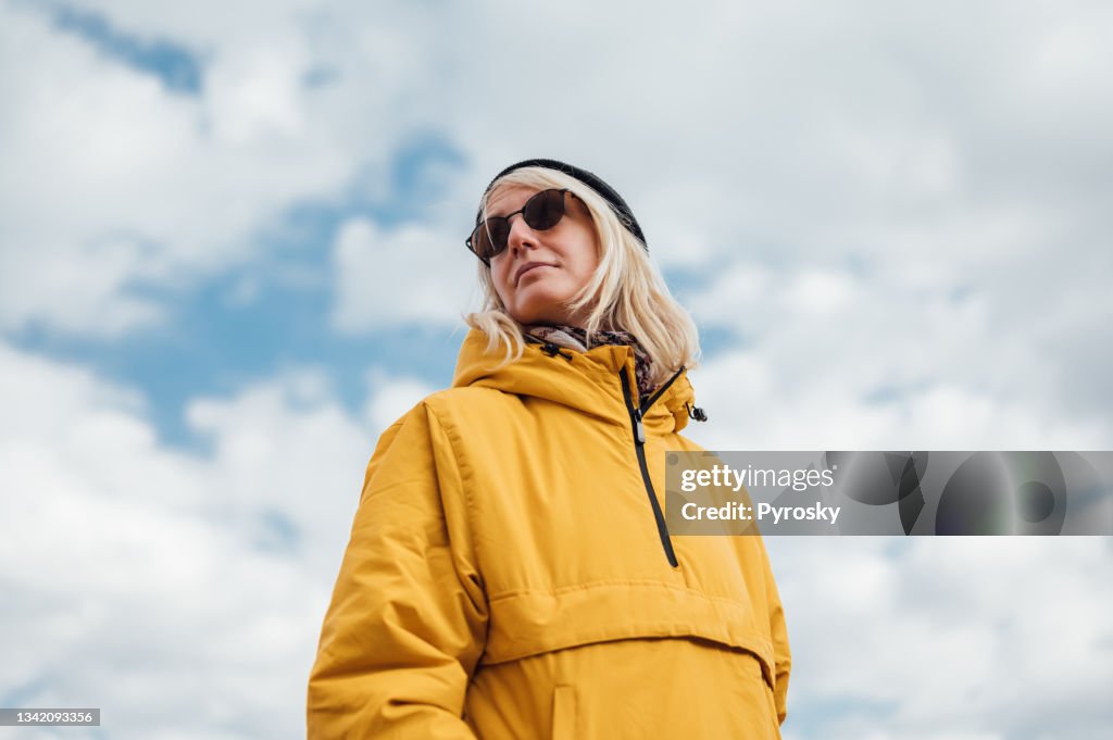 Eine urbane junge Frau in gelber Jacke gegen blauen Himmel 1