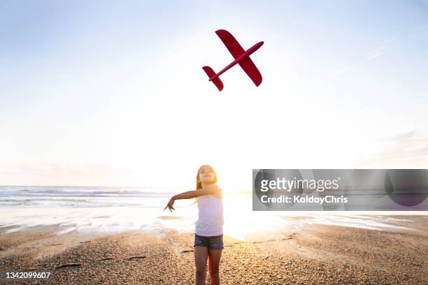 dream of flying in an airplane. girl running and playing with toy plane at sunset. girl on sunny background with plane in her hand. silhouette of girl throwing a toy plane into the sky - glider photos et images de collection