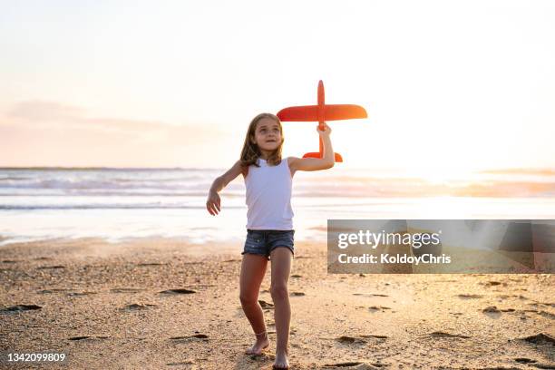 dream of flying in an airplane. girl running and playing with toy plane at sunset. girl on sunny background with plane in her hand. silhouette of girl throwing a toy plane into the sky - girl blowing sand stock-fotos und bilder