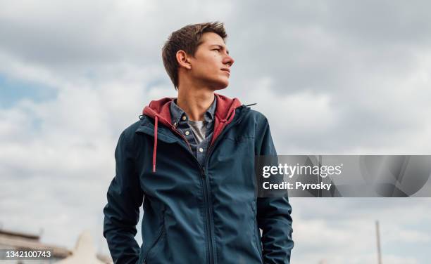 an urban young man in a blue jacket against a blue cloudy sky - garden in the cloud stock pictures, royalty-free photos & images