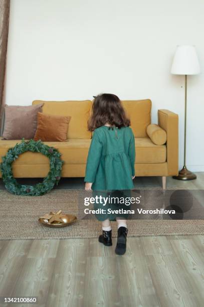 toddler girl in green linen suit and a headband walks near christmas decorations and the yellow fabric sofa at home. christmas outfit. preparing for celebration. festive season. lifestyle portrait. - green coat foto e immagini stock