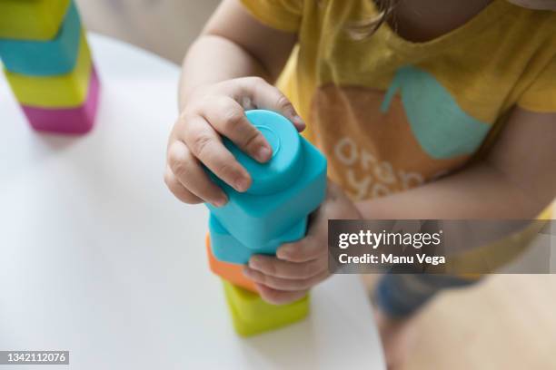 from above cropped unrecognizable cute infant girl playing with colorful plastic pyramid tower in nursery stacking blocks together - nursery stock pictures, royalty-free photos & images