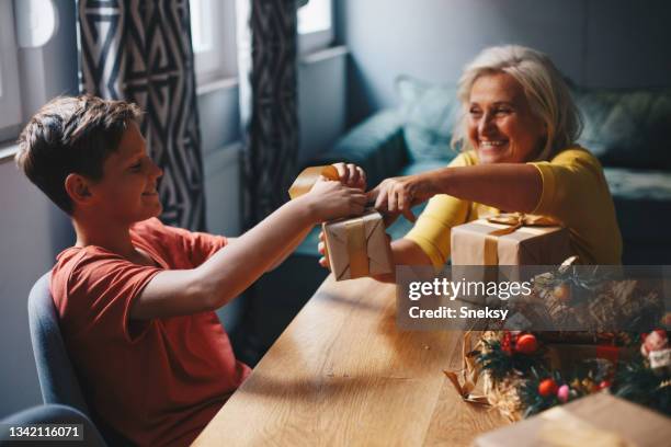 der kleine junge sitzt mit seiner oma am tisch und packt geschenke für neujahr und weihnachten. - 63 year old female stock-fotos und bilder