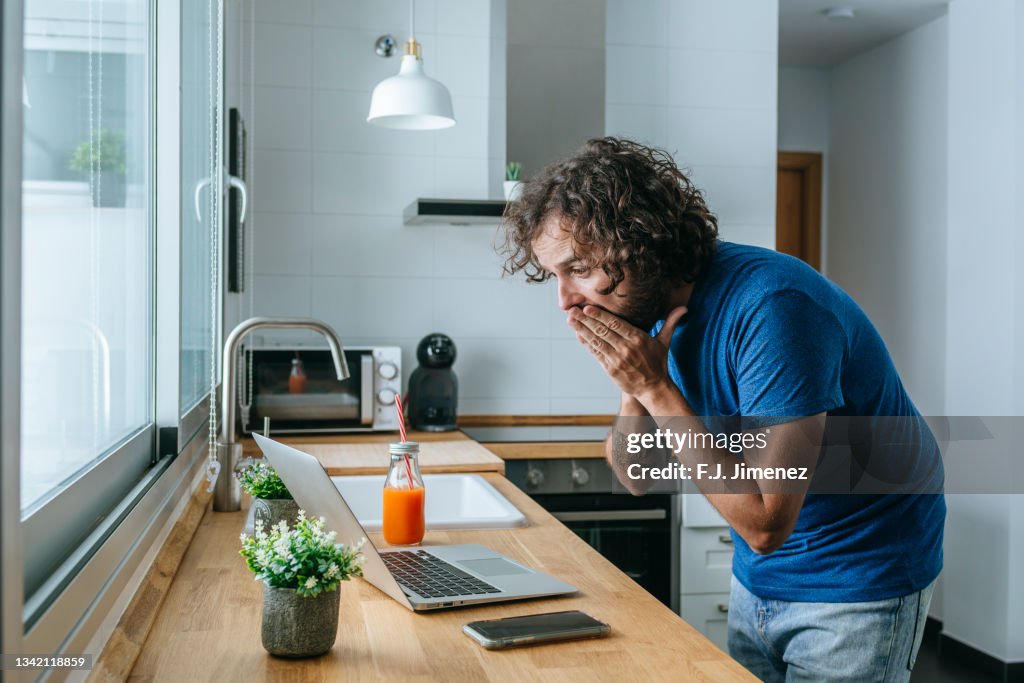 Man looking at laptop surprised at home
