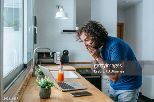 man looking at laptop surprised at home - man disbelief stock pictures, royalty-free photos & images