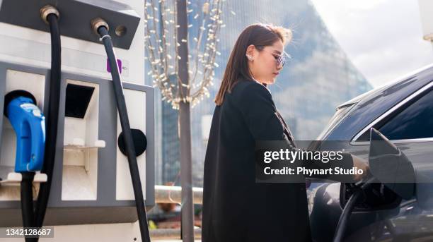 young woman charging an electric car at public charging station and pays using a mobile phone. innovative eco-friendly vehicle - car mobile stockfoto's en -beelden