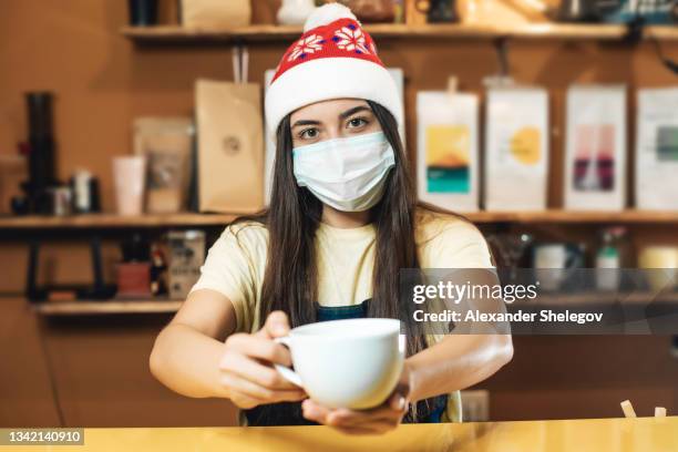 ritratto femminile di donna al chiuso che lavora come barista in un bar. la ragazza indossa il berretto rosso di babbo natale per natale e capodanno. foto con mascherina durante la pandemia covid-19 - ready to wear foto e immagini stock