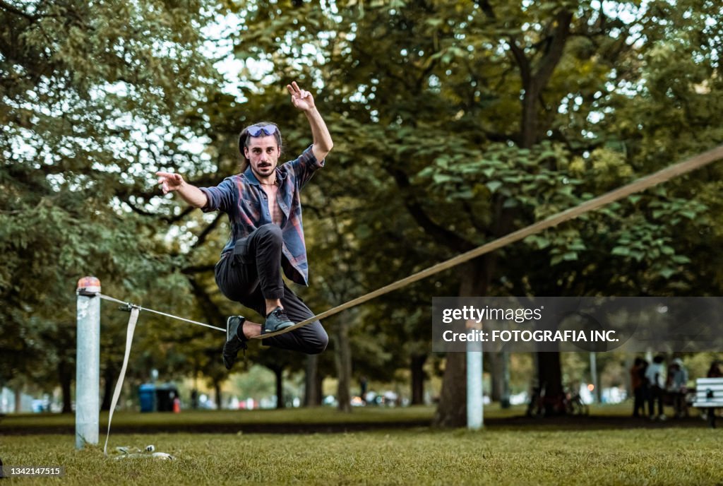 Junger Mann, der Acro Yoga auf Slackline im Park praktiziert