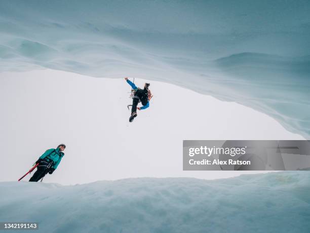 looking up at a mountain climber jumping across a deep crevasse - crevasse fotografías e imágenes de stock