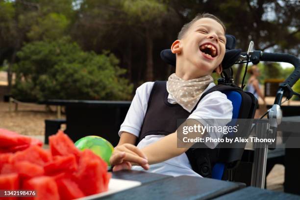 little 9s boy with cerebral palsy sit in wheelchair outdoor and laughing - cerebal palsy stockfoto's en -beelden