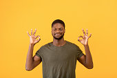 Stress relief concept. Young black man meditating with closed eyes, keeping calm on yellow studio background