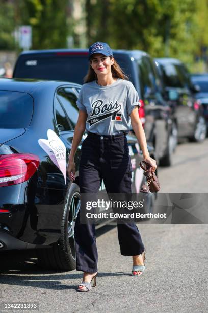 Gala Gonzalez wears navy blue with Boss slogan embroidered cap, a pale gray t-shirt with black and white Boos slogan print pattern, a brown shiny...