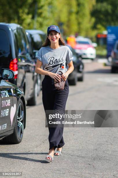 Gala Gonzalez wears navy blue with Boss slogan embroidered cap, a pale gray t-shirt with black and white Boos slogan print pattern, a brown shiny...