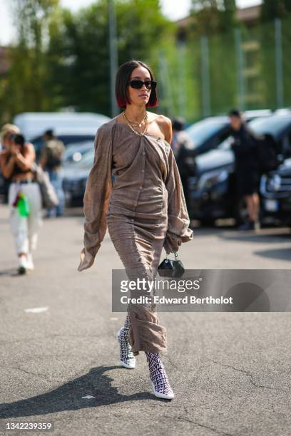 Alexandra Guerain wears black sunglasses, gold chain necklaces, a brown linen buttoned / puffy long sleeves/ long tube dress, a black shiny leather...