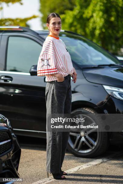 Maeva Marshall wears gold earrings, a white latte with red stripes oversized sport baseball teams t-shirt from Boss, black faded denim large jeans...