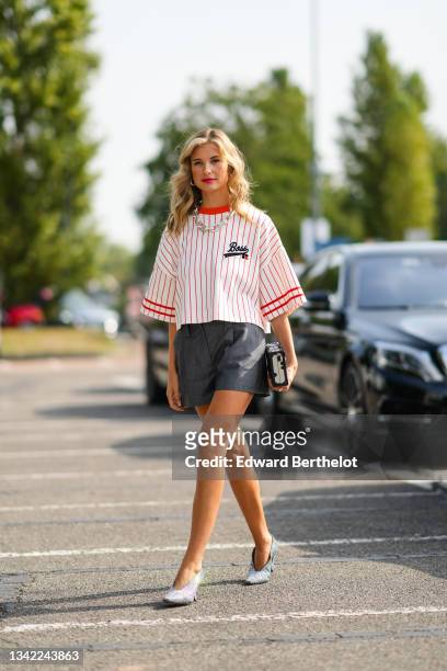 Xenia Adonts wears silver large earrings, a silver large chain necklace, a white latte with red stripes oversized sport baseball teams t-shirt from...