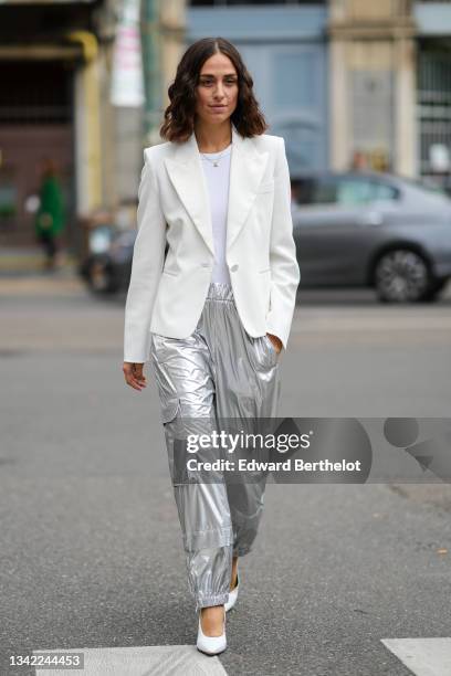 Erika Boldrin wears a white ribbed t-shirt, a gold chain pendant necklace, a white blazer jacket, silver shiny large cargo pants, white leather...
