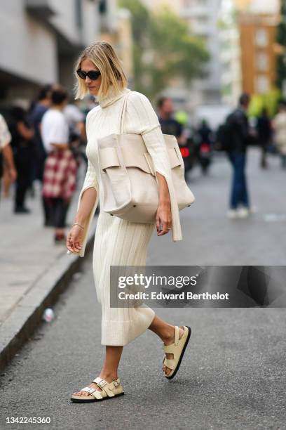 Linda Tol wears black sunglasses, a pale yellow ribbed wool turtleneck long cut-out sleeves midi dress, a beige fabric with a beige shiny leather...