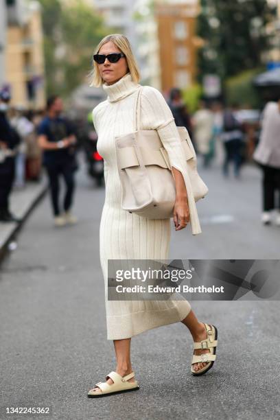 Linda Tol wears black sunglasses, a pale yellow ribbed wool turtleneck long cut-out sleeves midi dress, a beige fabric with a beige shiny leather...