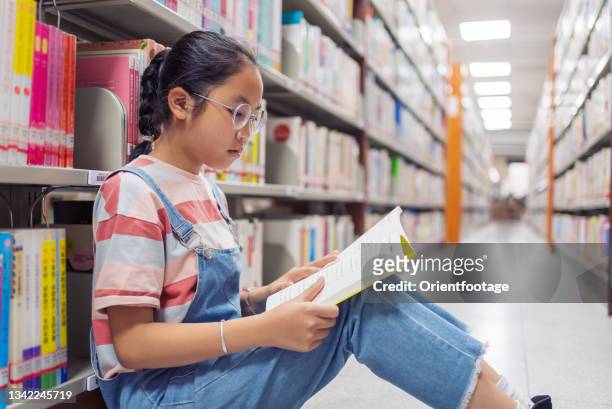 little girl reading a book on bookshelf in the library - girl reading stock pictures, royalty-free photos & images